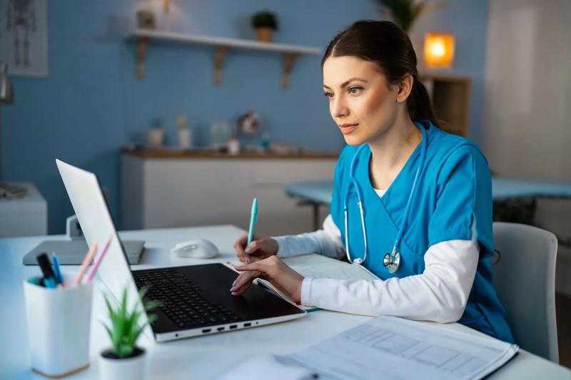 Female medical student in blue medical scrubs, e-learning on a laptop at the ordination