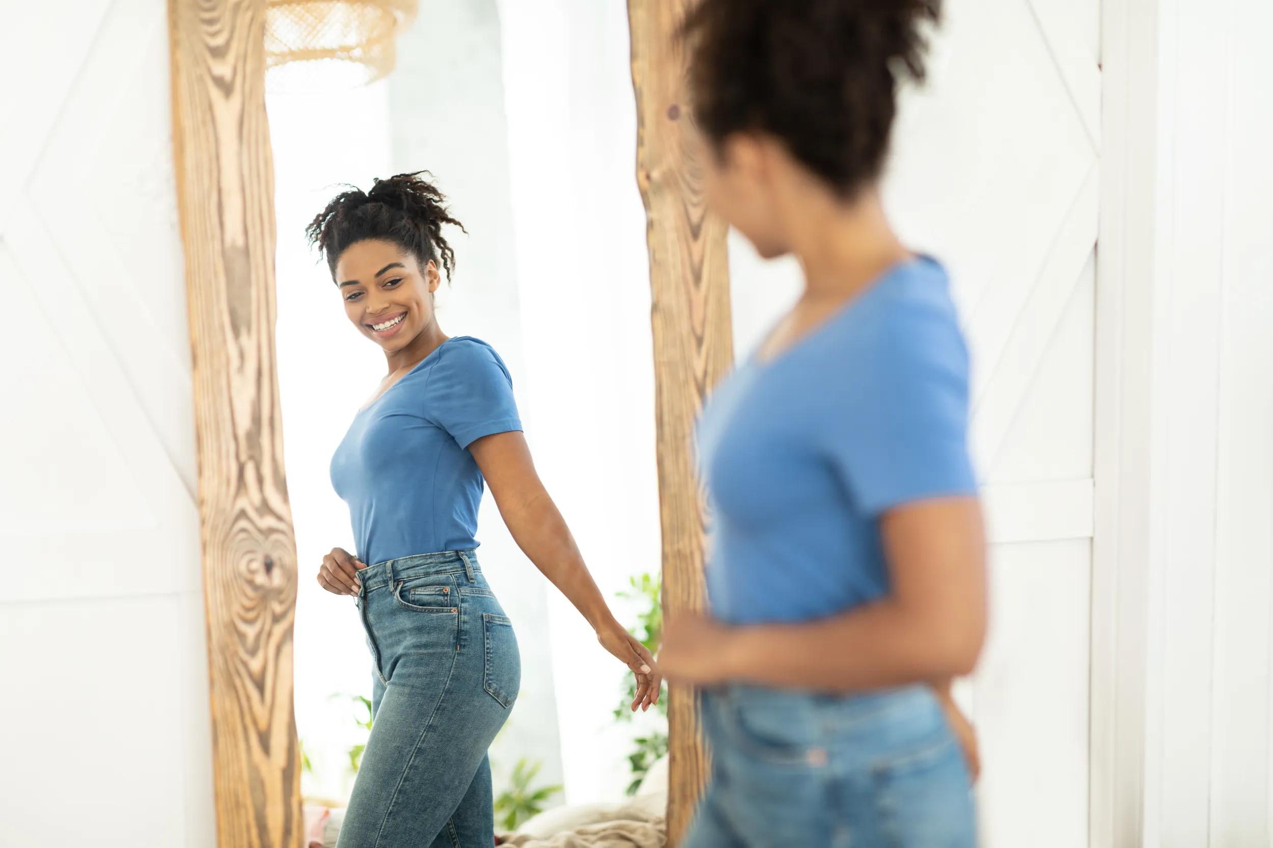 Cheerful Slim Black Girl Looking At Reflection In Mirror Indoor