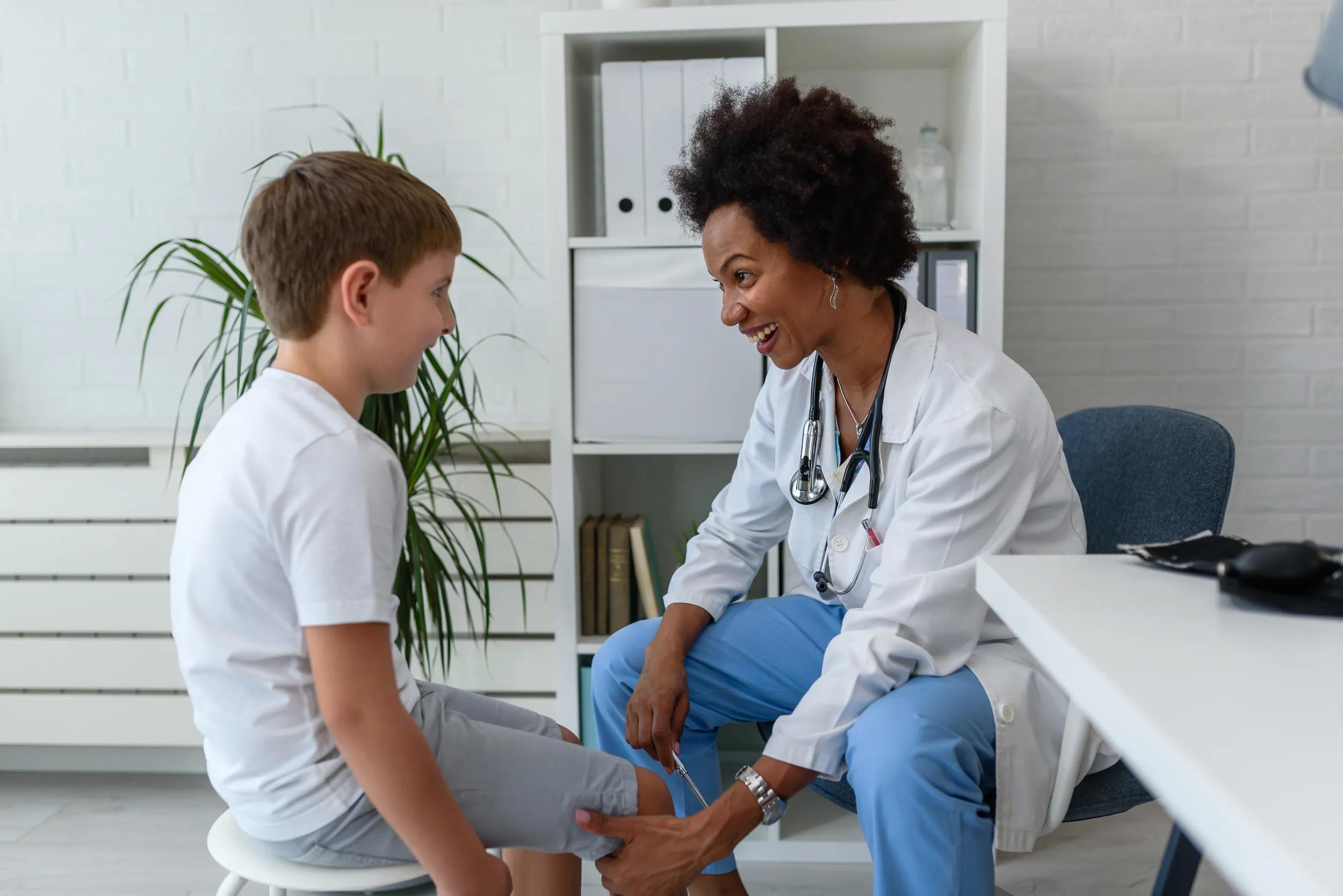 Woman African American doctor general practitioner examining child's patellar knee-jerk reflex