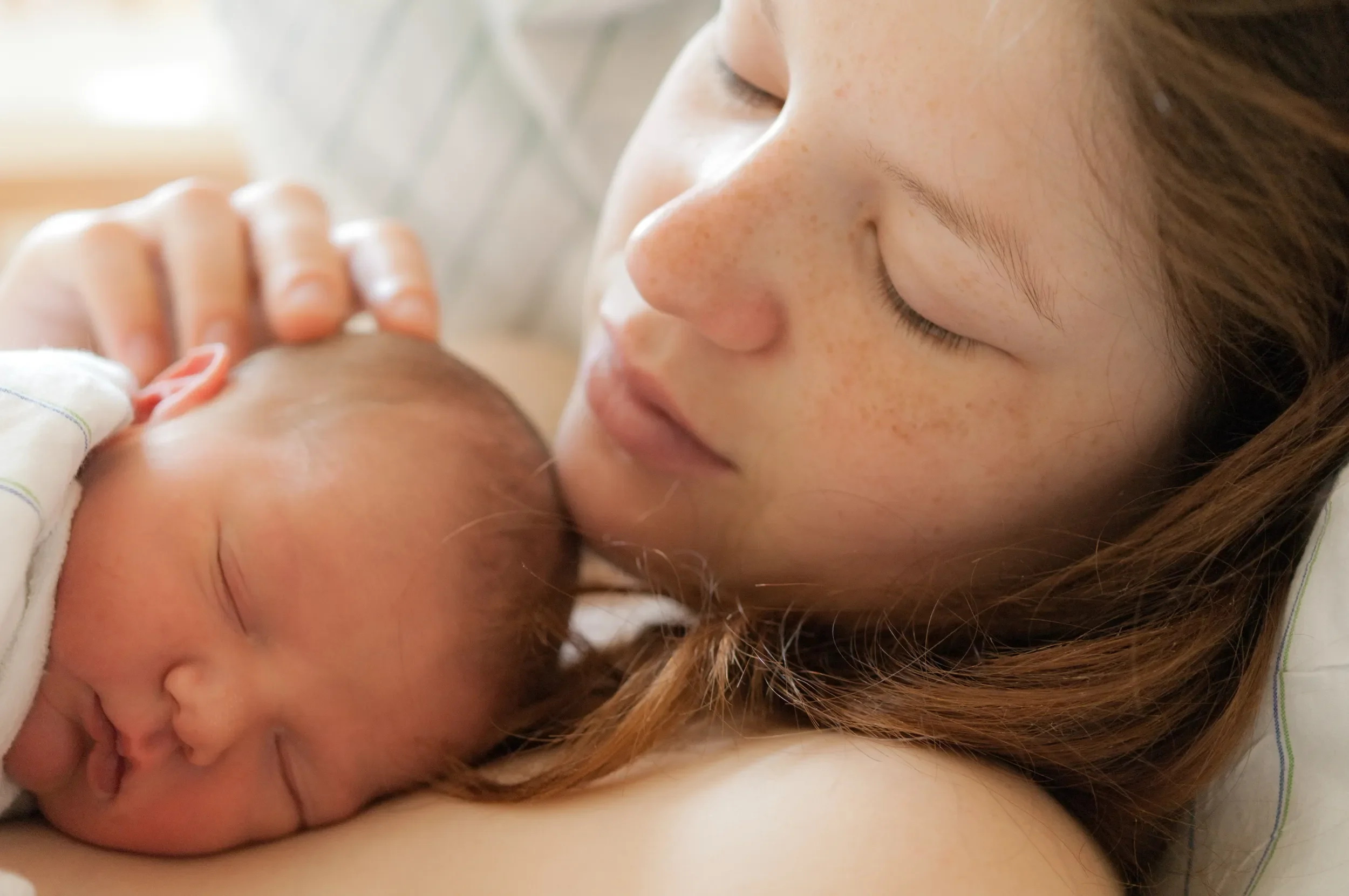 Sleeping Baby on her mother's chest. Both have their eyes closed.