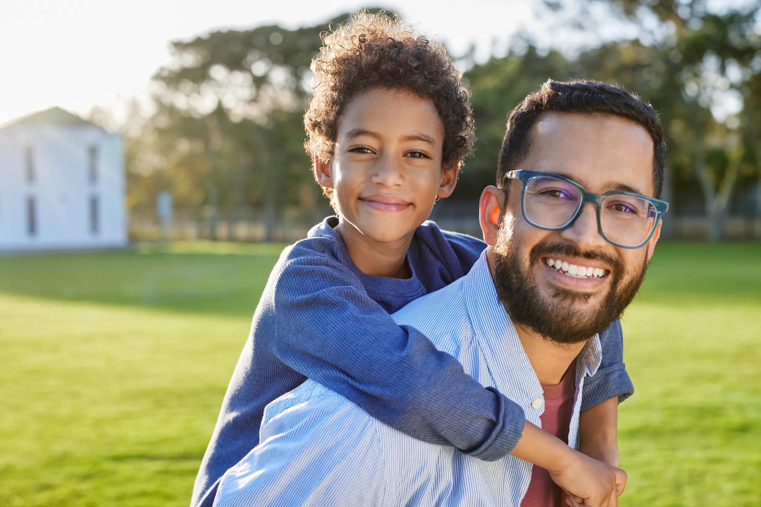 Happy hispanic father piggyback his son at park