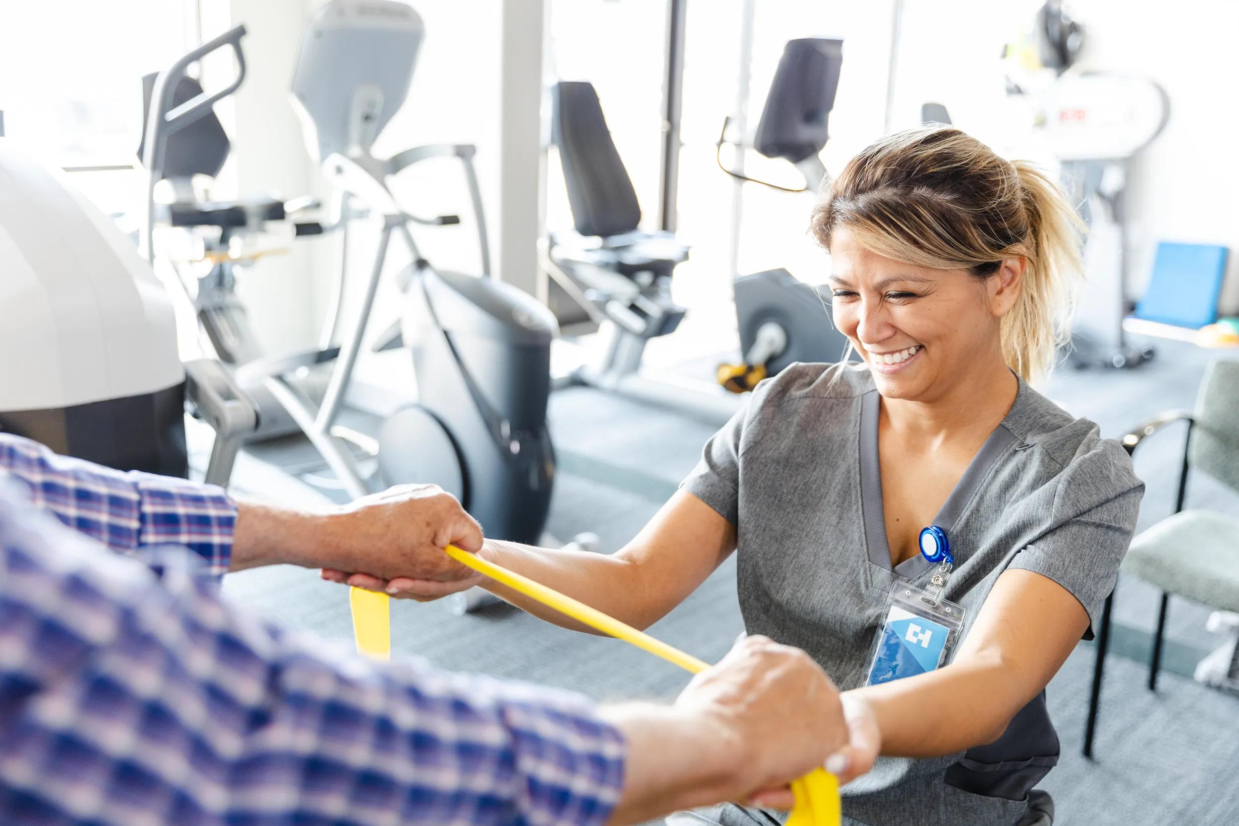 Cheerful female occupational therapist helps senior man with resistance band