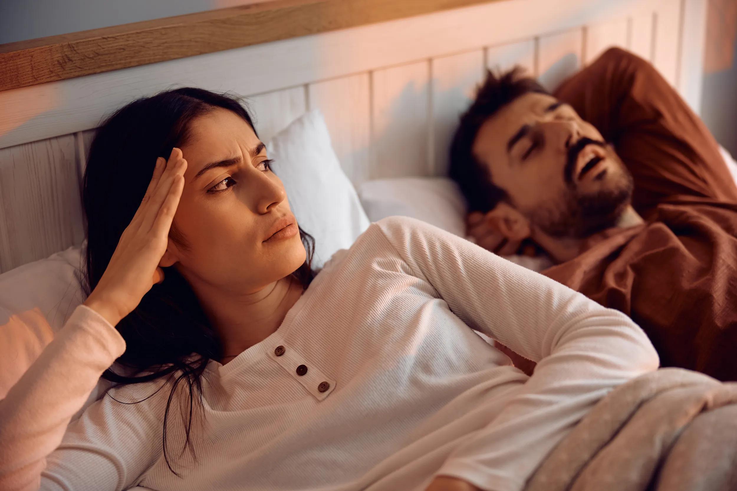 Young woman feeling frustrated about her boyfriend's snoring in bedroom.