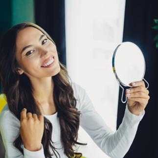 Young brunette woman at home smiles while looking into a round mirror in a bright living room