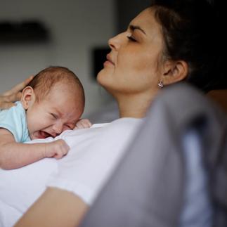 Exhausted mother holding her crying newborn baby. Postpartum depression.
