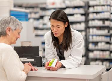 Asian Pharmacist Assists Elderly Customer At Pharmacy Counter Providing Medication Guidance