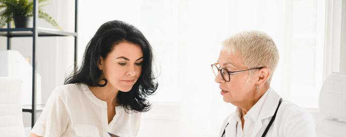 Radiogram. Caucasian senior female doctor general practitioner showing x-ray lungs photo to female patient, explaining diagnosis, symptoms at hospital