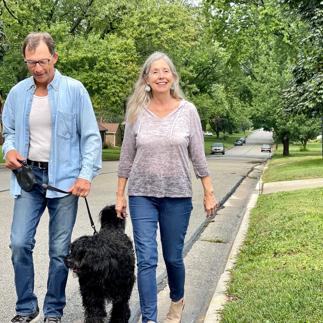 Senior couple out for a walk with pet Portuguese water dog on tree lined street in neighborhood.