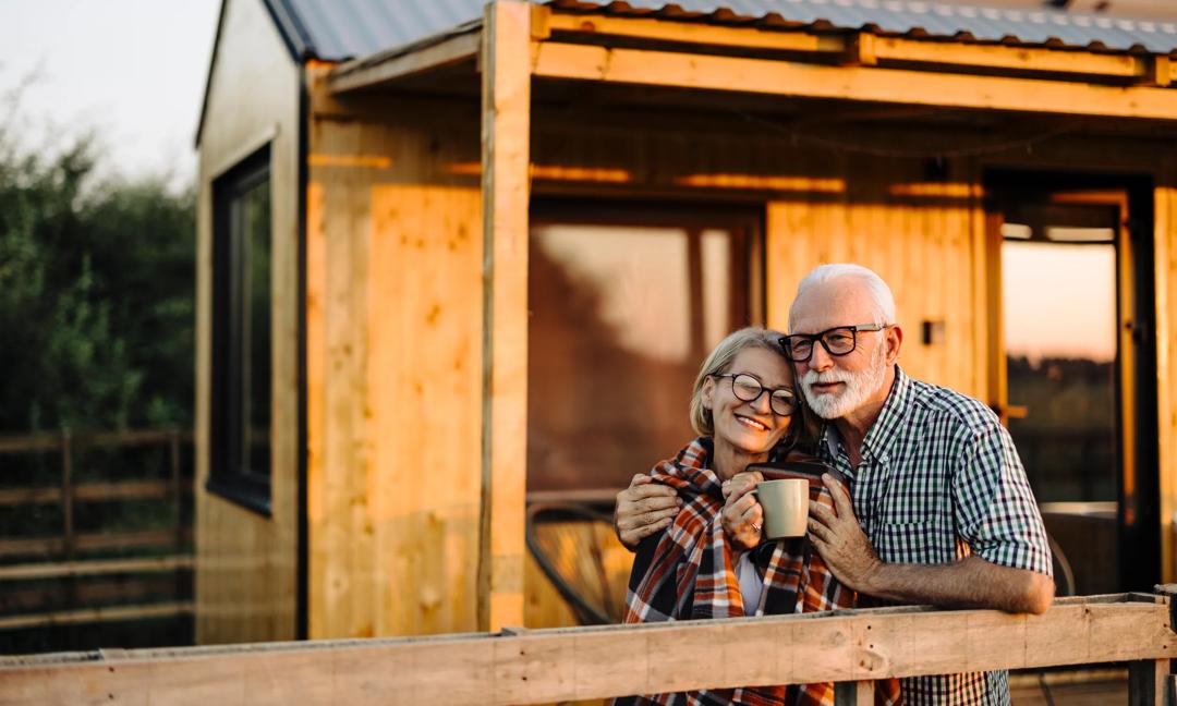 Happy senior couple is on their vacation and spending the evening on the cabin patio, keeping warm with a blanket and a cup of coffee