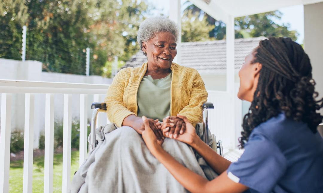 Young female nurse holding hands with an elderly patient in a wheelchair