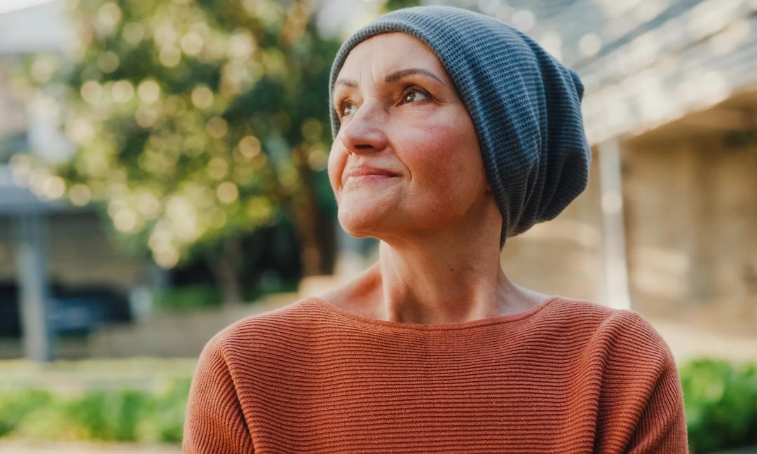 Senior woman cancer patient with headscarf walking relax enjoy the warmth of sunlight and fresh air therapy recovery in the park. Living with cancer concept.