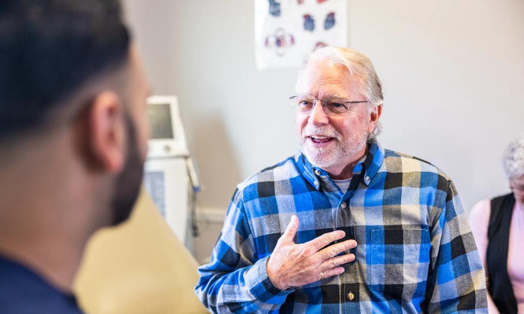 Senior man speaking with doctor in the exam room with his wife in the background