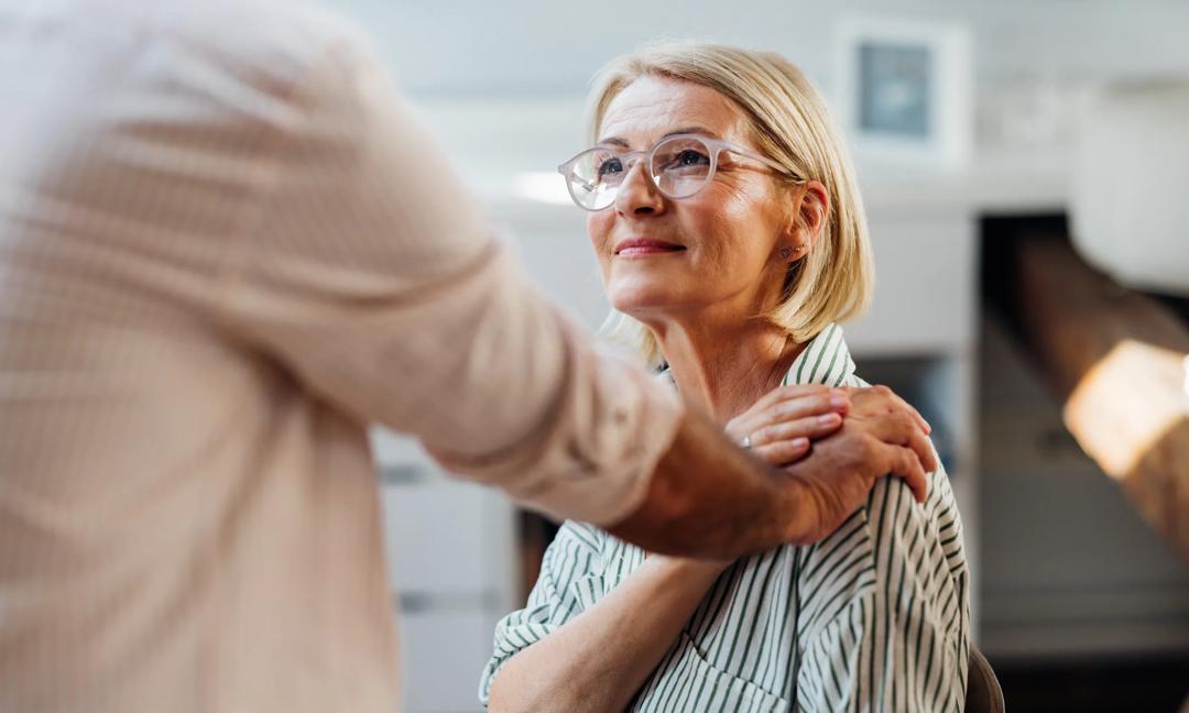 Senior Woman Supported by Male Friend in Modern Home Interior