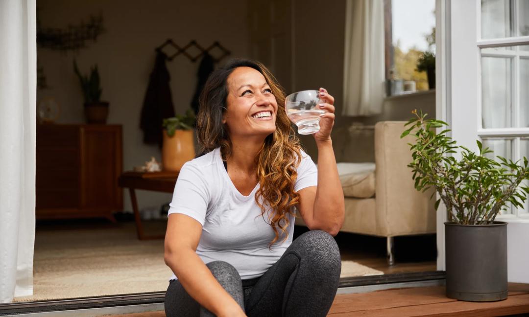 Smiling mature woman sitting on her patio drinking water