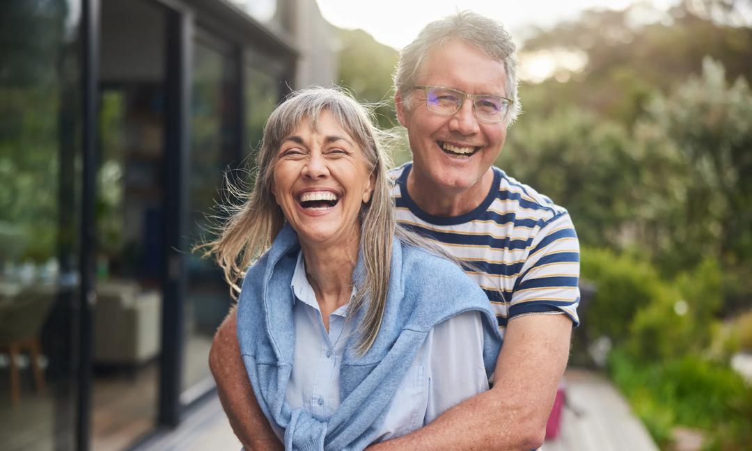 Mature couple standing arm in arm and laughing outside in summer