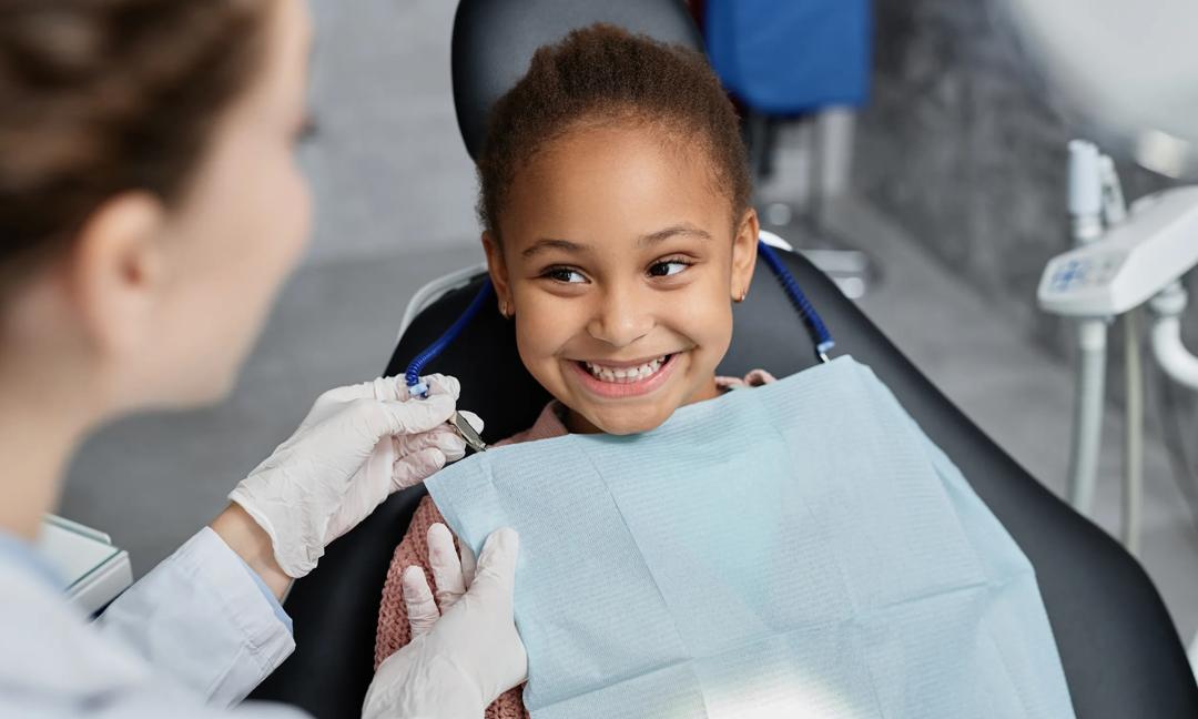 Smiling little girl in dental chair with nurse preparing her for teeth check up