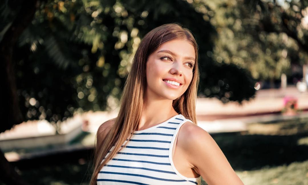 Smiling young woman in striped top enjoying a sunny summer day outdoors  natural portrait of happiness and relaxed lifestyle in a park setting
