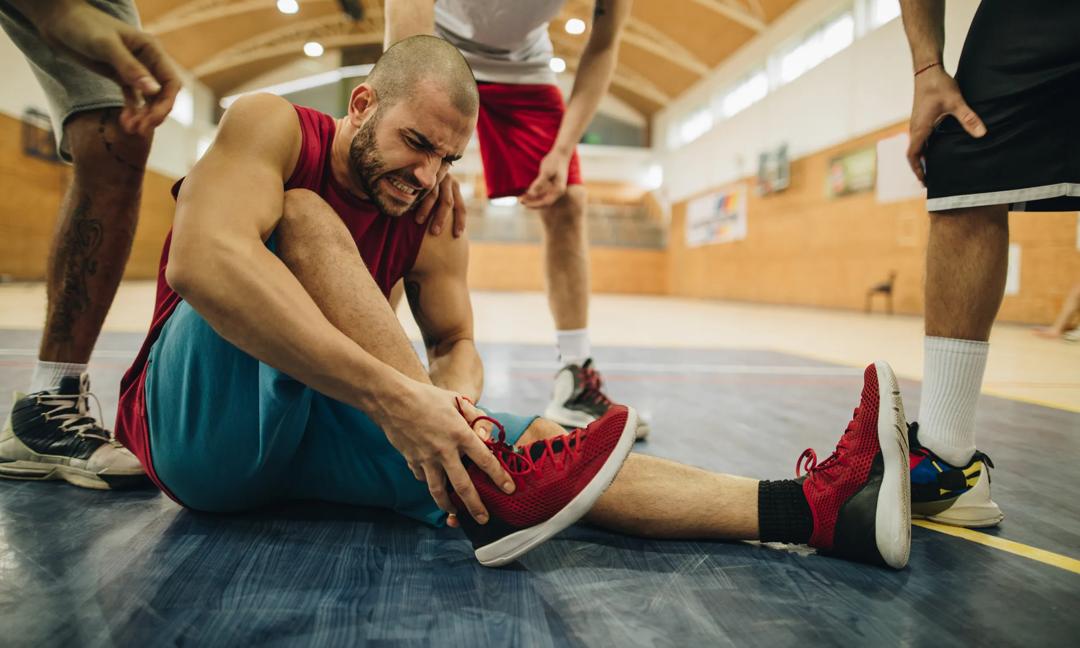 Injured basketball player holding his ankle in pain on the court.