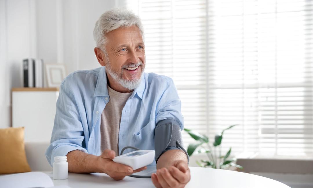 Senior man measuring blood pressure at table indoors