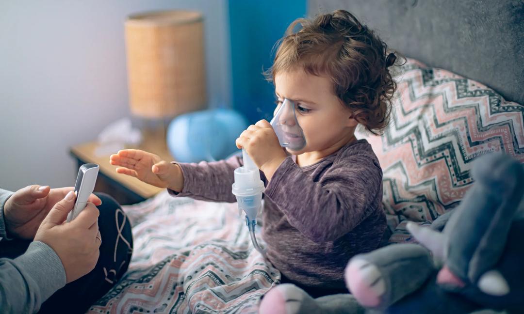 Mother helping her little daughter doing inhalation with a nebulizer