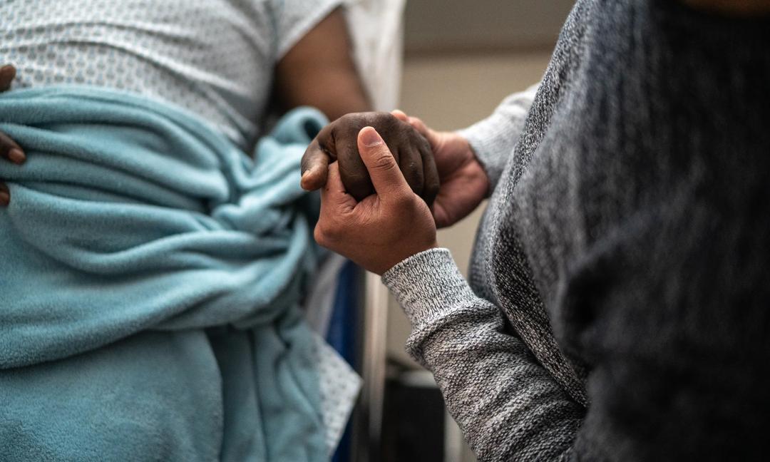 Son holding father's hand at the hospital