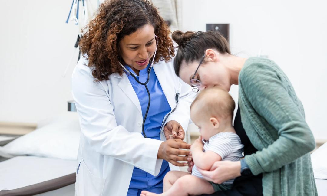 Doctor using stethoscope to check a baby's heartbeat. Mother comforts child.