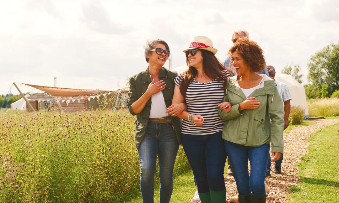 Group Of Smiling Mature Friends Walking Along Path Through Yurt Campsite