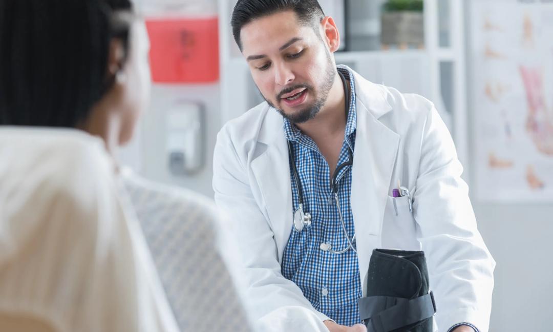 Serious doctor helps female patient with orthopedic boot