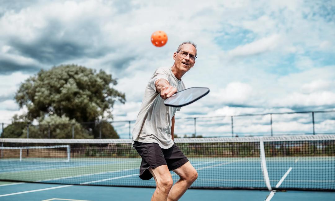 Active senior man playing pickleball on outdoor court