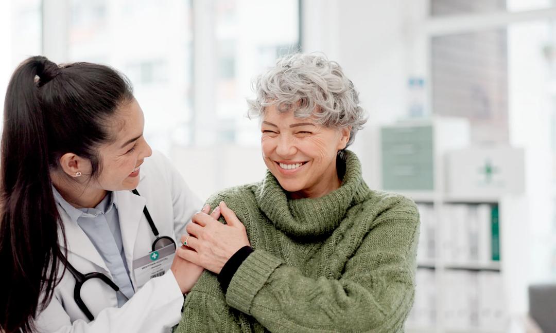 Happy, care and face of a doctor with a woman for medical trust, healthcare and help. Laughing, hug and portrait of a young nurse with a senior patient and love during a consultation at a clinic