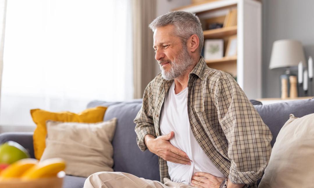 Man holding his stomach in pain while resting on the couch.