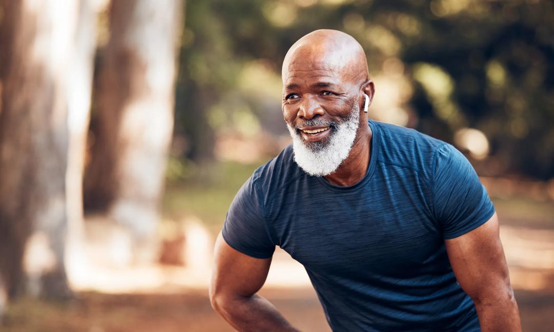 Black man, break from running and relax with fitness, vitality and cardio, senior runner in the park. Exercise, earpods and listen to music for motivation, tired with endurance and health outdoor