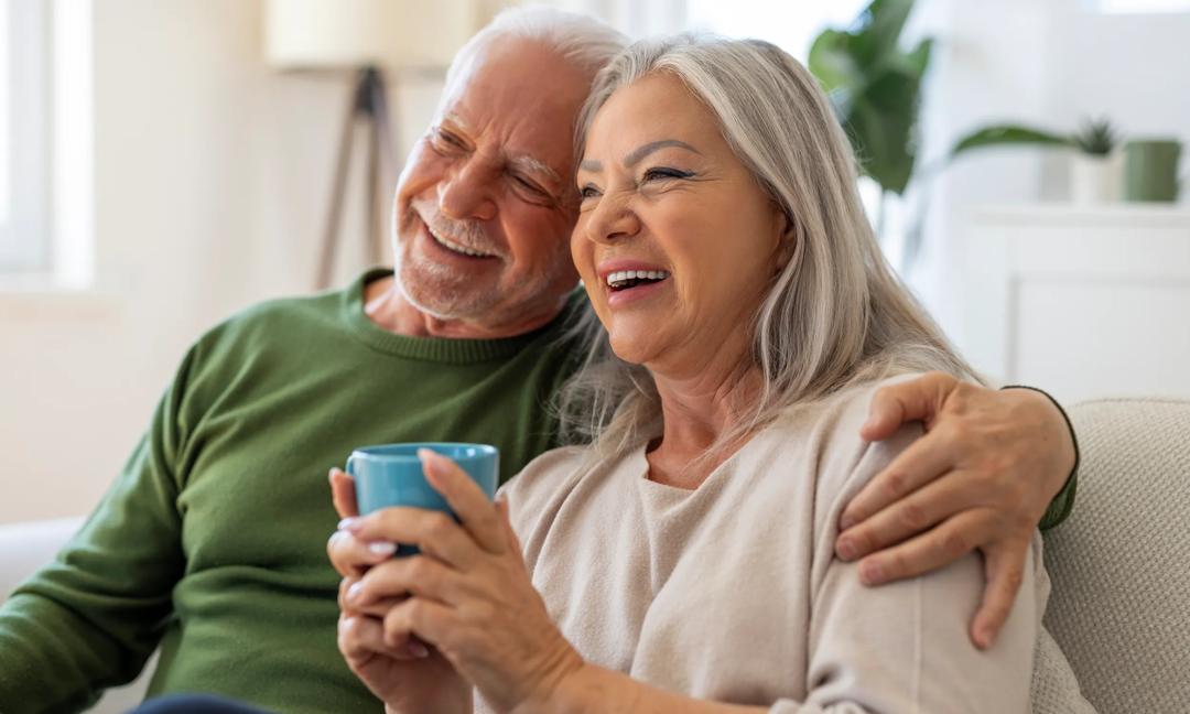 Happy Senior Couple Relaxing on Sofa with Coffee at Home