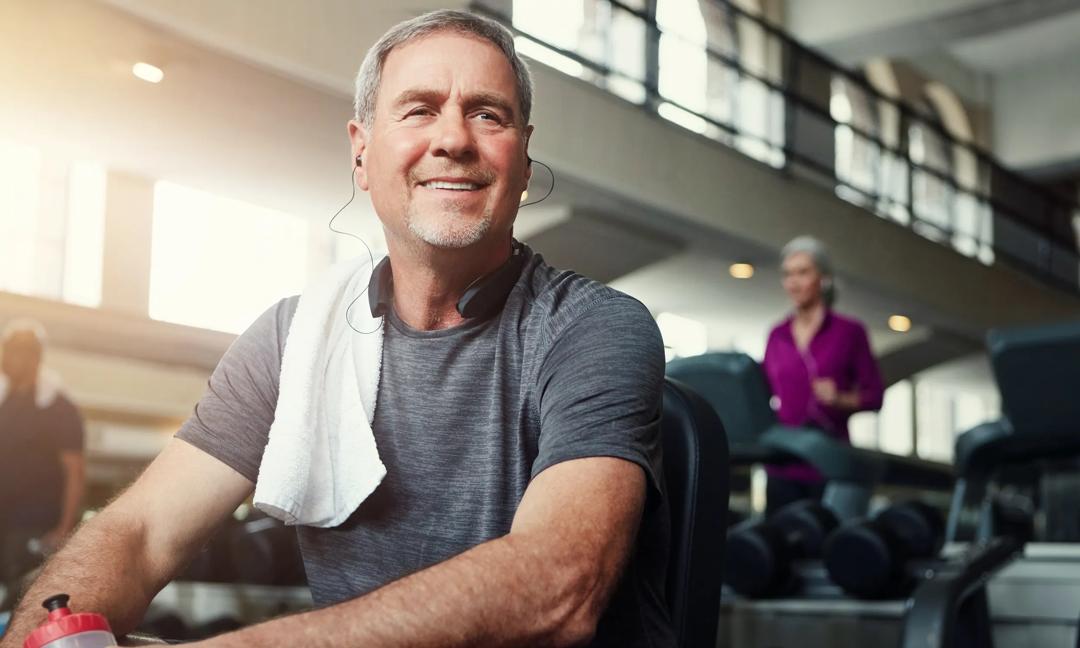 Fitness, headphones and old man relax in gym with water bottle for training, exercise and workout. Sports, retirement and person listening to audio, podcast or music for wellness, health and resting