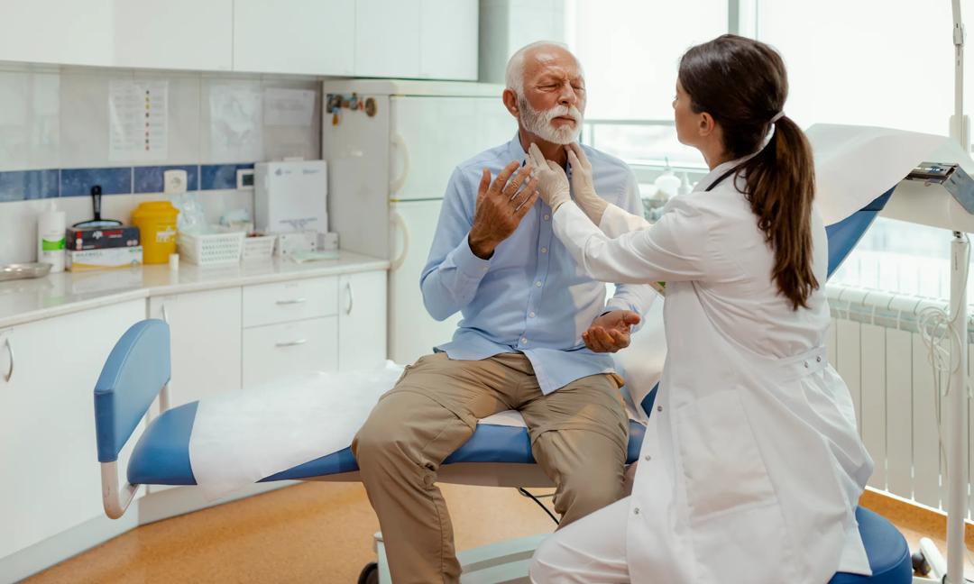 Female physician performs clinical neck checkup on mature male patient. Screening for goiter, swelling, or early signs of thyroid condition.