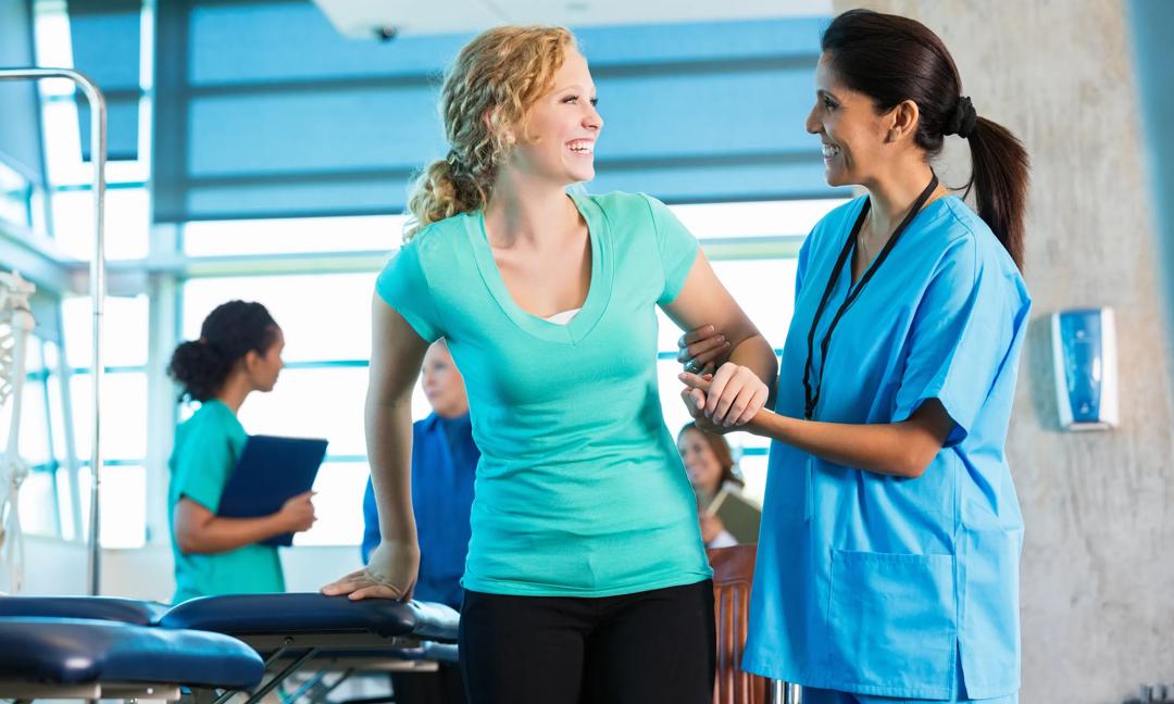 Mature physical therapist helping injured teenage girl to walk