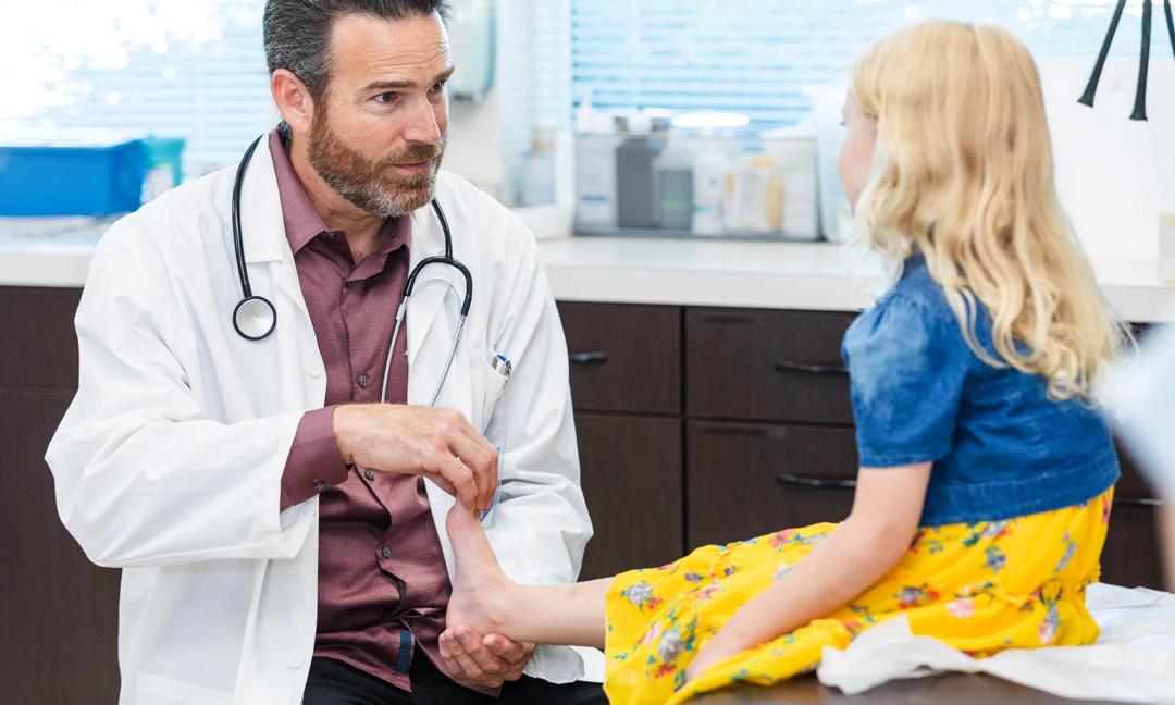 Male doctor asks unrecognizable girl about pain in foot