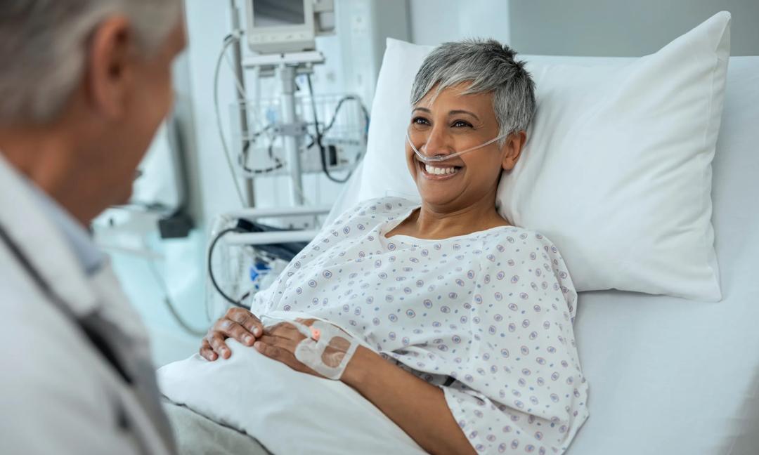 Doctor, senior woman and talking in bed with smile for good news, wellness and results in hospital. Medic, consulting and mature patient with advice, happy and medical review for recovery in clinic