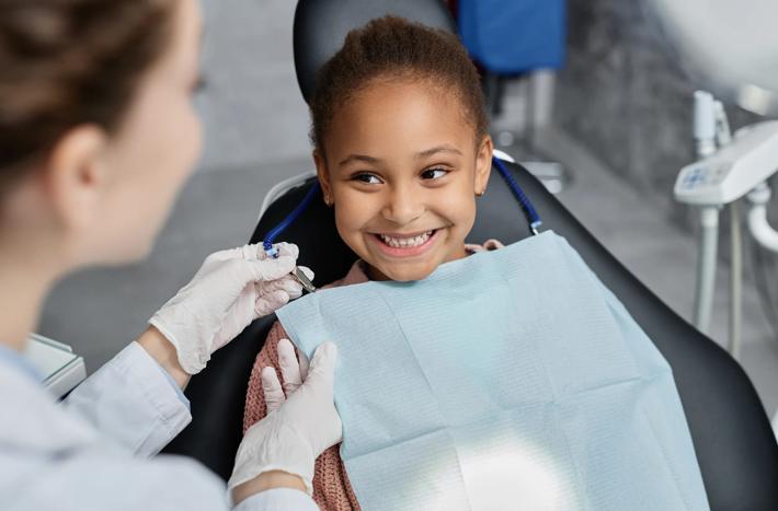Smiling little girl in dental chair with nurse preparing her for teeth check up