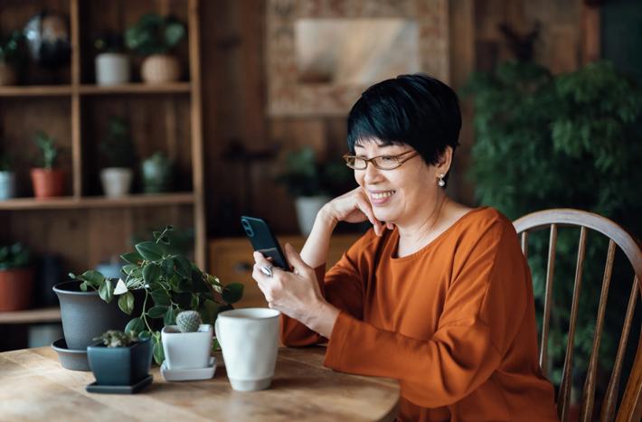 Smiling senior Asian woman managing online banking with mobile app on smartphone, taking care of her money and finances while relaxing at home. Retirement lifestyle. Elderly and technology