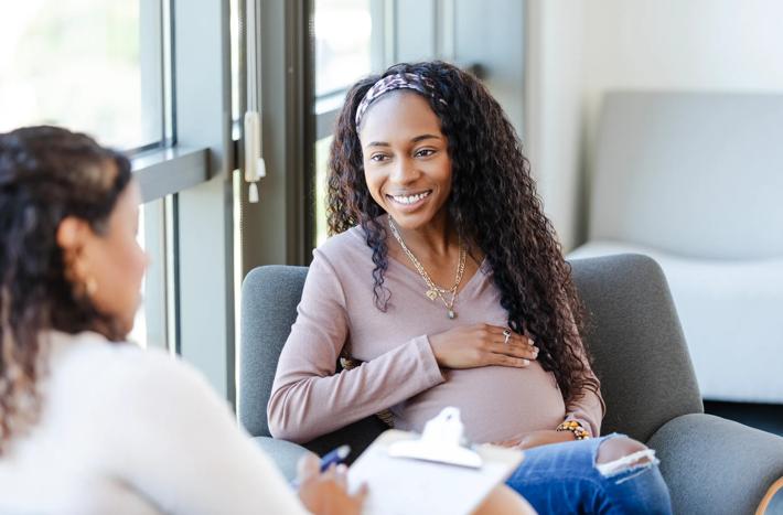 The expectant young adult woman smiles as she listens to advice from her unrecognizable female counselor.