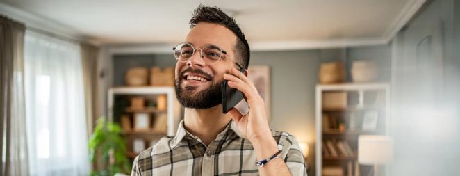 A handsome man with a beard is having a pleasant conversation on the phone at home